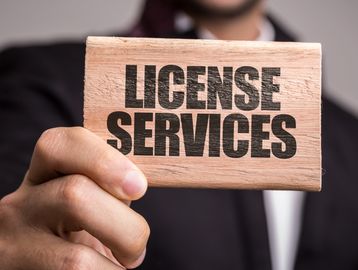 A person holding a wooden block with "LICENSE SERVICES" text.