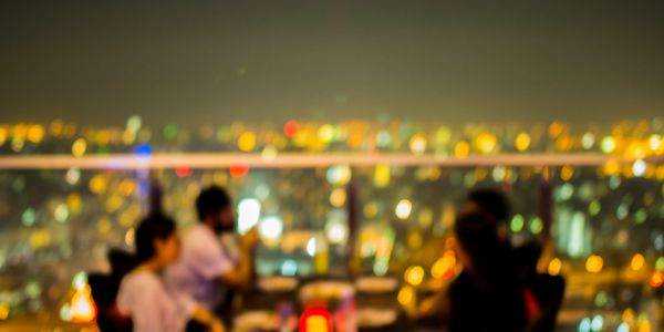 Blurry night city view with people at a rooftop table.