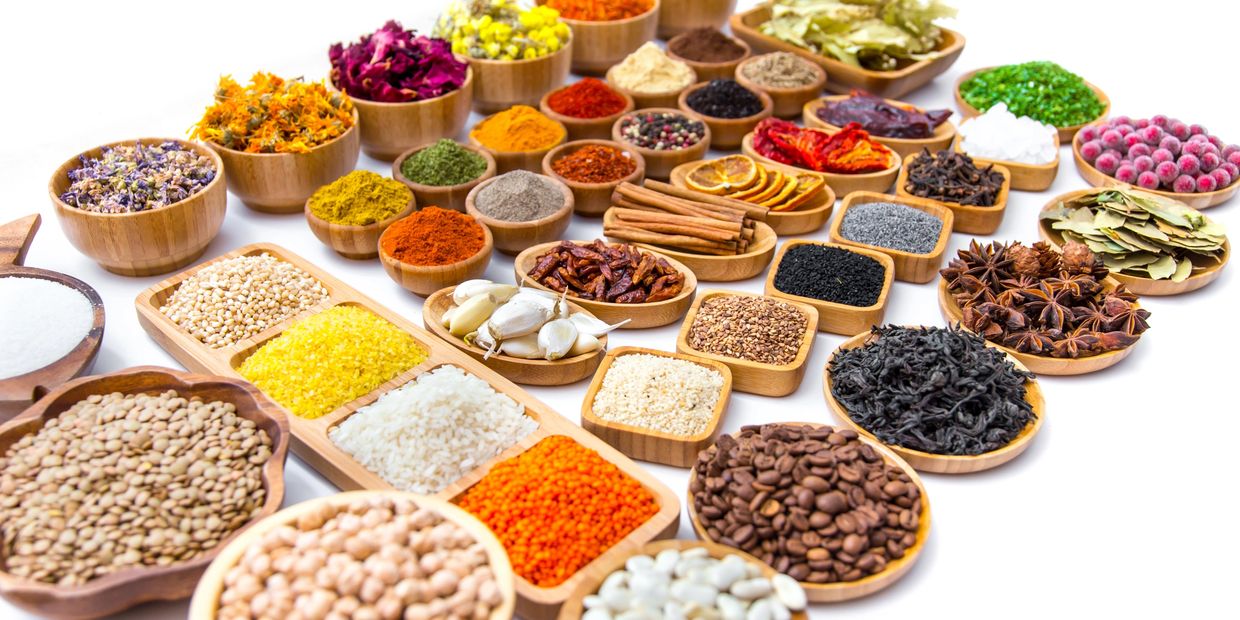 A vibrant assortment of spices, herbs, seeds, and dried goods in wooden bowls.