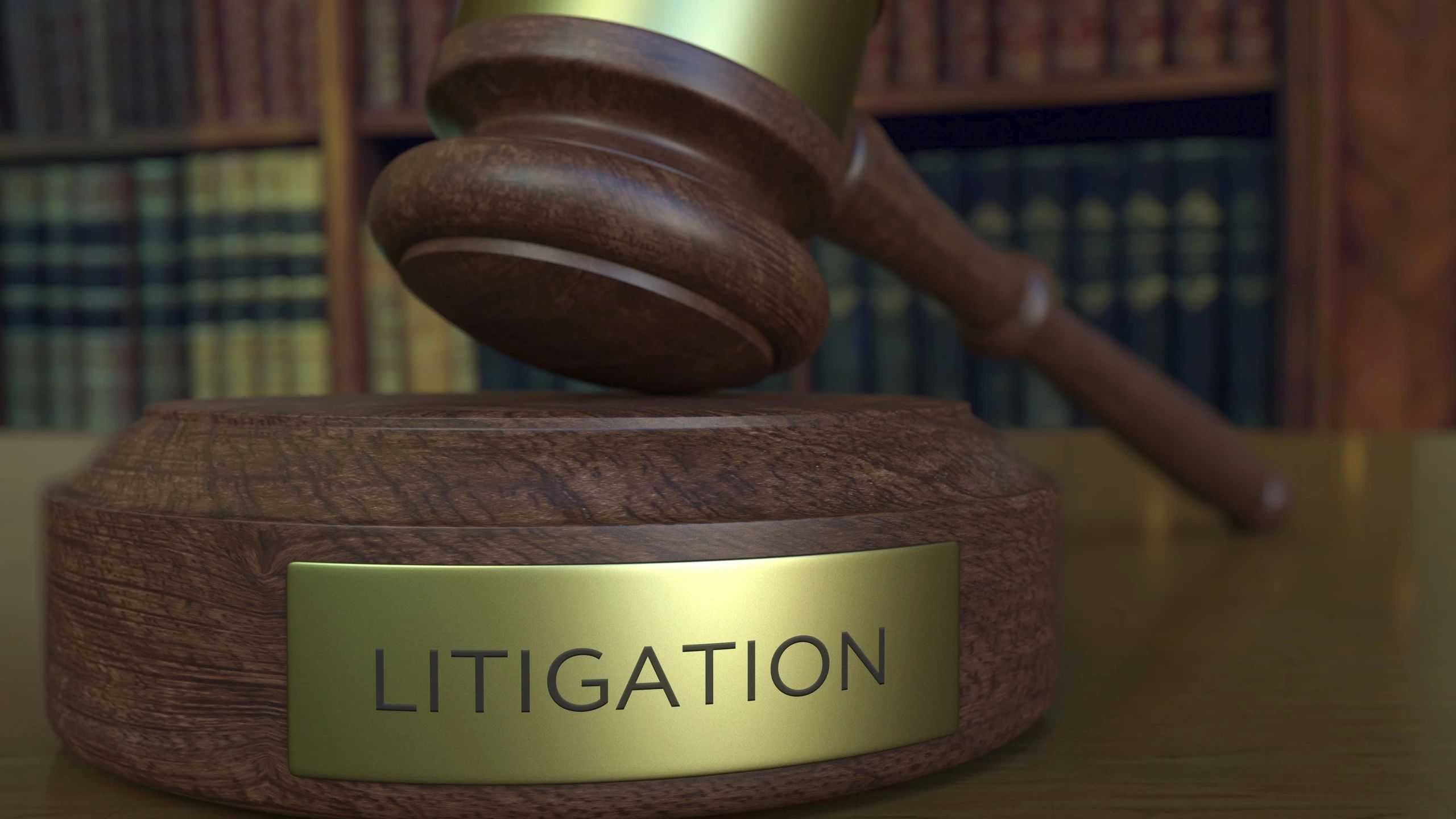 Courtroom gavel with the word LITIGATION written on the wooden base and law books in the background.