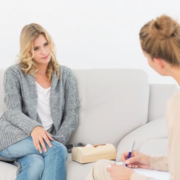 A woman attentively listens during a therapy session on a couch.