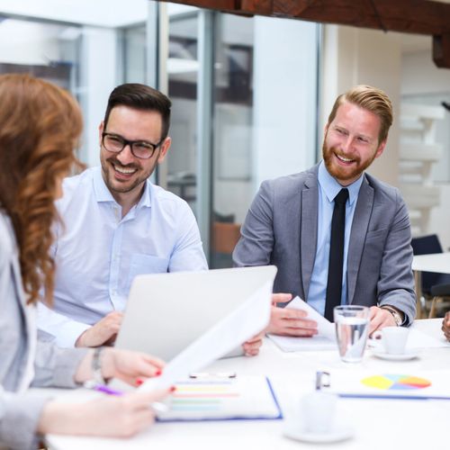 Three colleagues smiling and discussing work in a modern office.