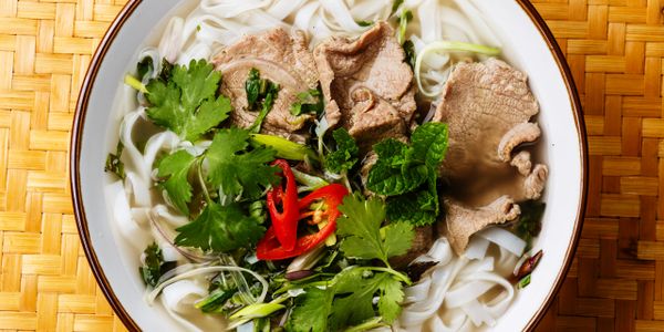 Bowl of Vietnamese pho with beef, herbs, and noodles.