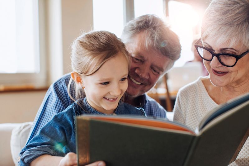 Grandparents reading a book to their beautiful granddaughter at home.