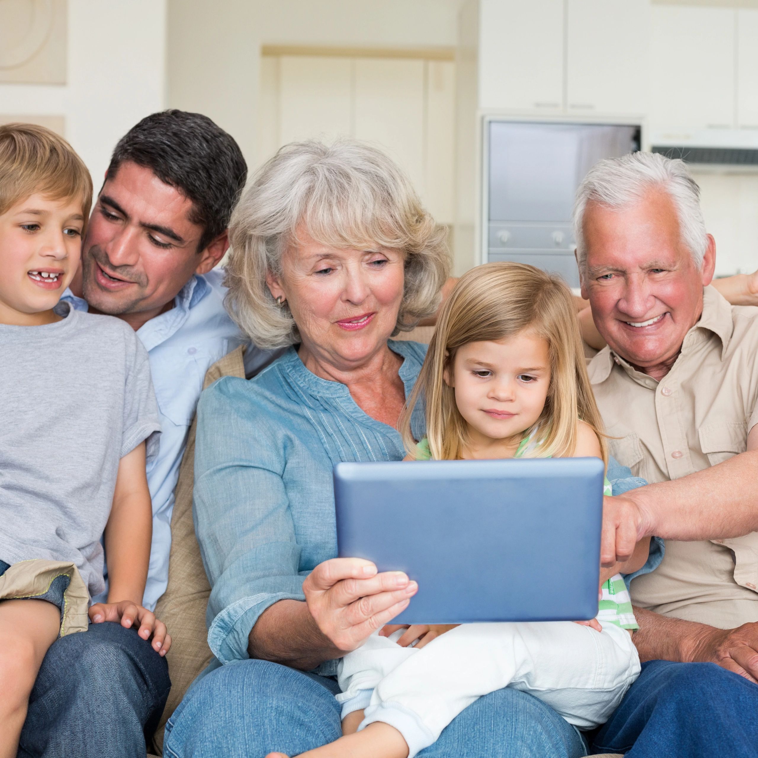 A family of grandparents, son and two young grandchildren smiling looking at a tablet screen.