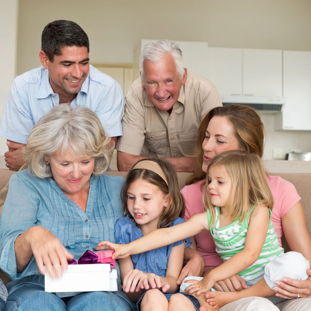Multi-generational family joyfully opening gifts together in a cozy home setting.