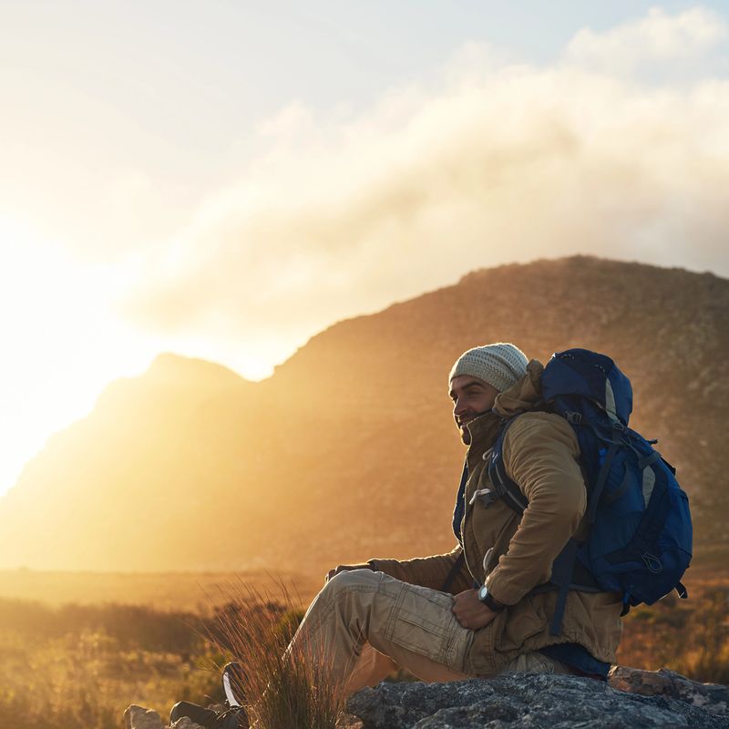 Shot of a hiker sitting on top of a mountain smiling