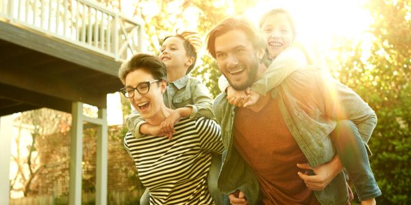 Family enjoying piggyback rides outdoors in the sunshine.