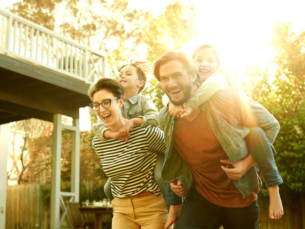 Happy family enjoying piggyback rides outdoors in the sunset.