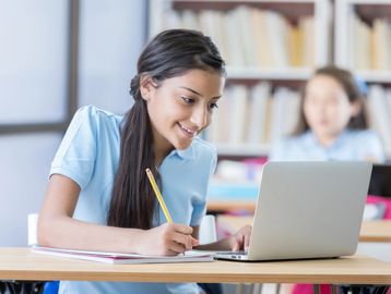 A student smiling while working on a laptop in a classroom.