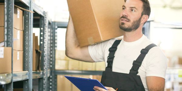 Worker holding a cardboard box and clipboard in a warehouse.