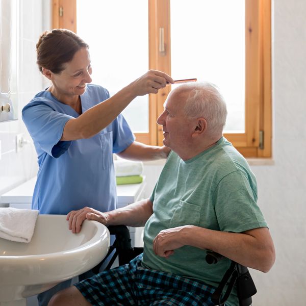Caregiver combing elderly man's hair in bathroom.