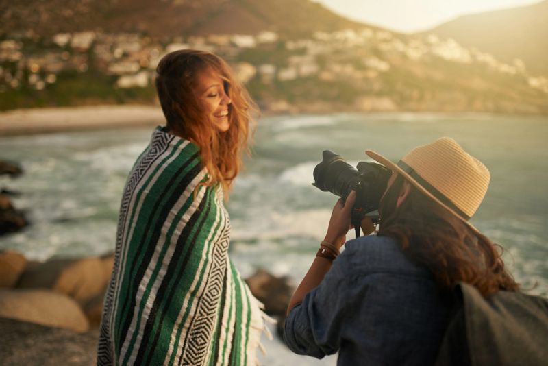 Shot of a happy young woman photographing her friend in front of a sea view