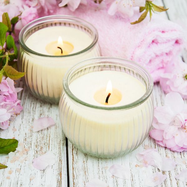 Two lit candles with pink flowers and a towel on a white wooden surface.