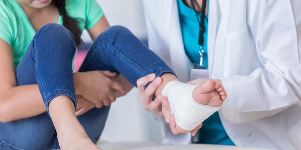 Doctor bandaging a young girl's ankle injury in a clinic.
