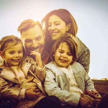 Happy family of four smiling together in warm sunlight outdoors.