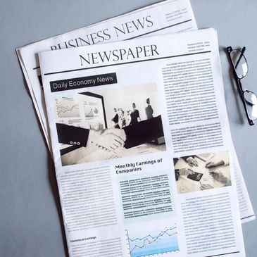 Business newspapers with articles and charts, accompanied by reading glasses.