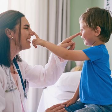 A female doctor and a young boy touch noses, sharing a joyful moment.