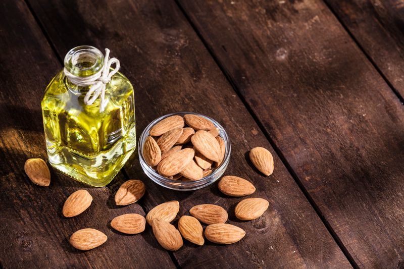 High angle view of a little glass bowl filled with peeled almonds and an open glass bottle filled with almond oil beside it shot on rustic wood table