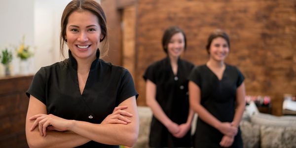 Three women in black uniforms smiling in a spa or wellness center.