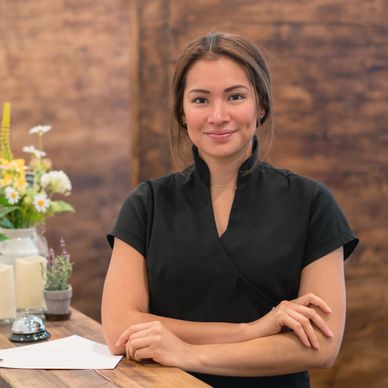 Smiling receptionist standing behind a wooden counter with flowers and candles.