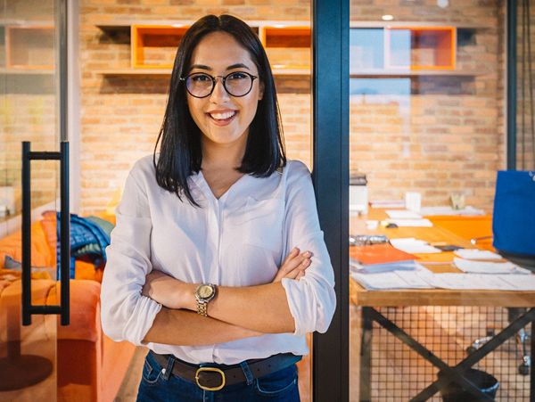 Confident young woman with glasses standing in a modern office.