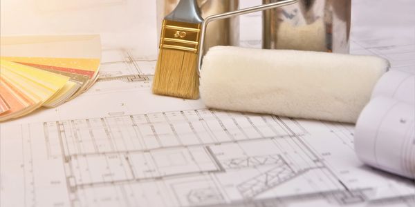 Paintbrush, roller, and color swatches on architectural blueprints.