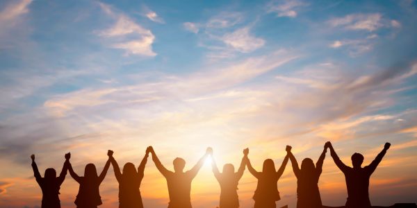 Silhouetted group holding hands at sunset with a colorful sky.