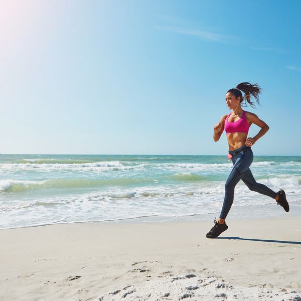 Woman jogging energetically on a sunny beach with ocean waves in the background.
