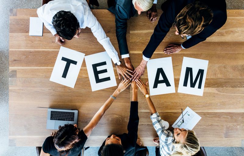 Group of business people putting their hands together over a table with work team. Top view of business team stacking hands.