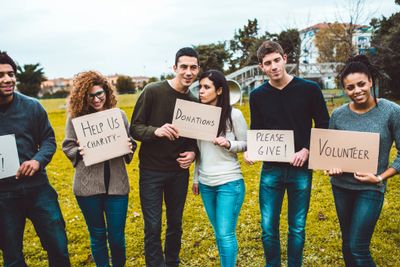 Group of young volunteers holding signs asking for donations and help.