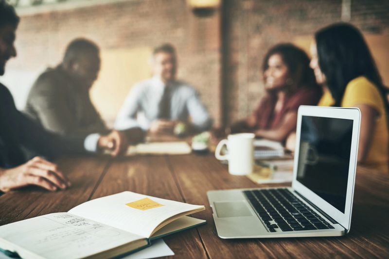 Shot of a laptop and paperwork on a boardroom table with unidentifiable businesspeople meeting in the background