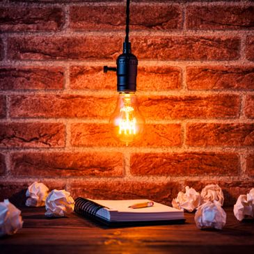 Glowing light bulb over a notebook and crumpled paper on a wooden table.