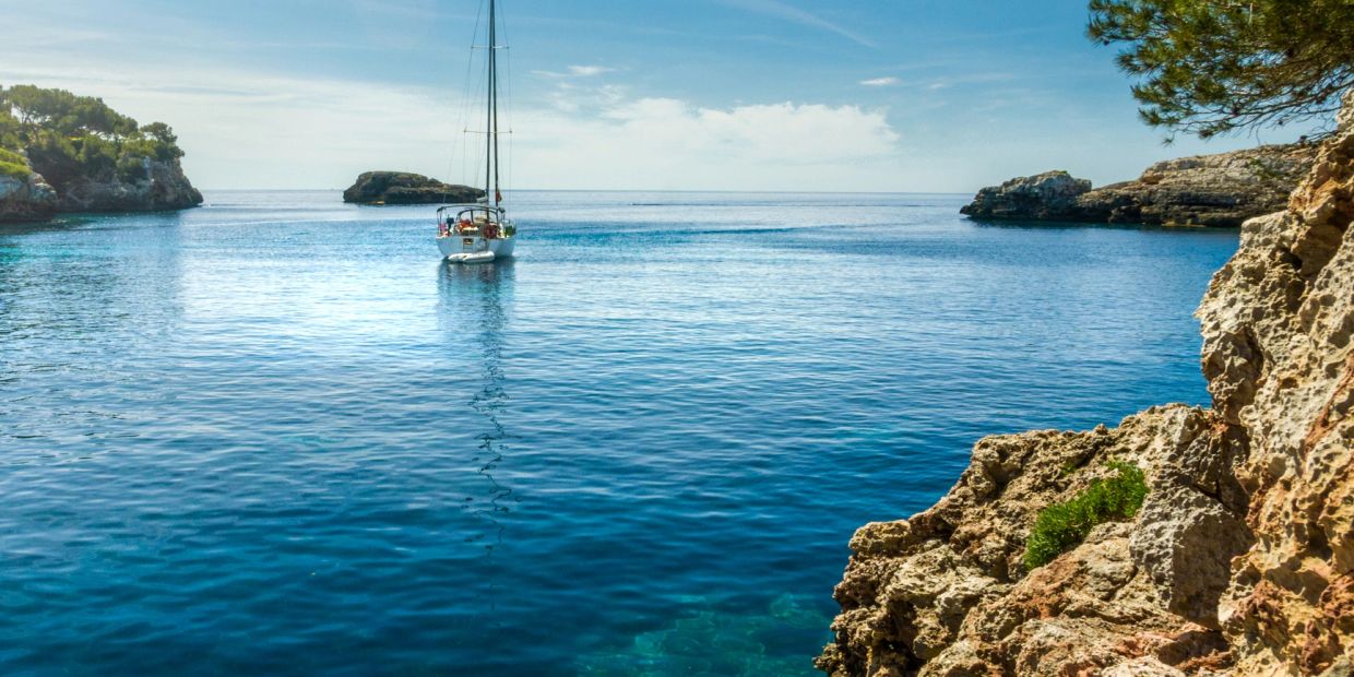 Sailboat on calm blue sea near rocky cliffs.