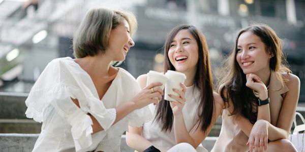 Three women laughing and enjoying coffee together outdoors.
