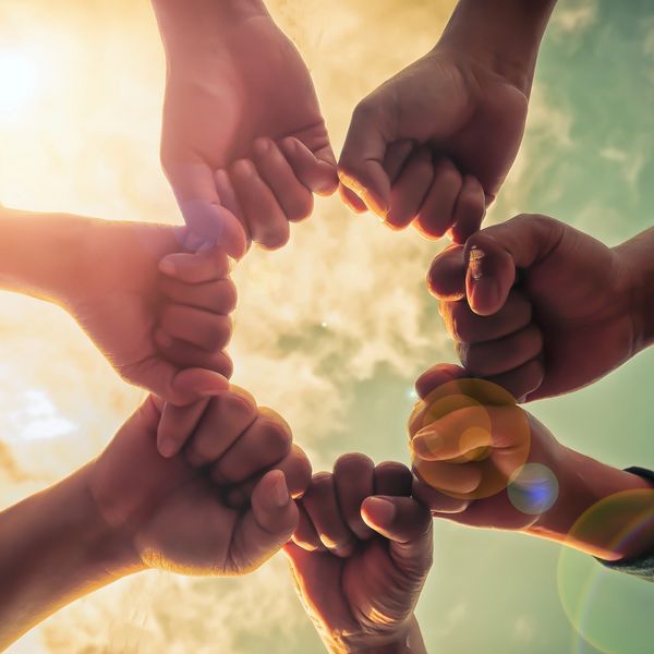 People linking pinkies in a circle with sunlight and sky background.