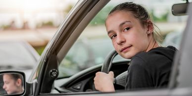 Young woman looking back while holding a car steering wheel.