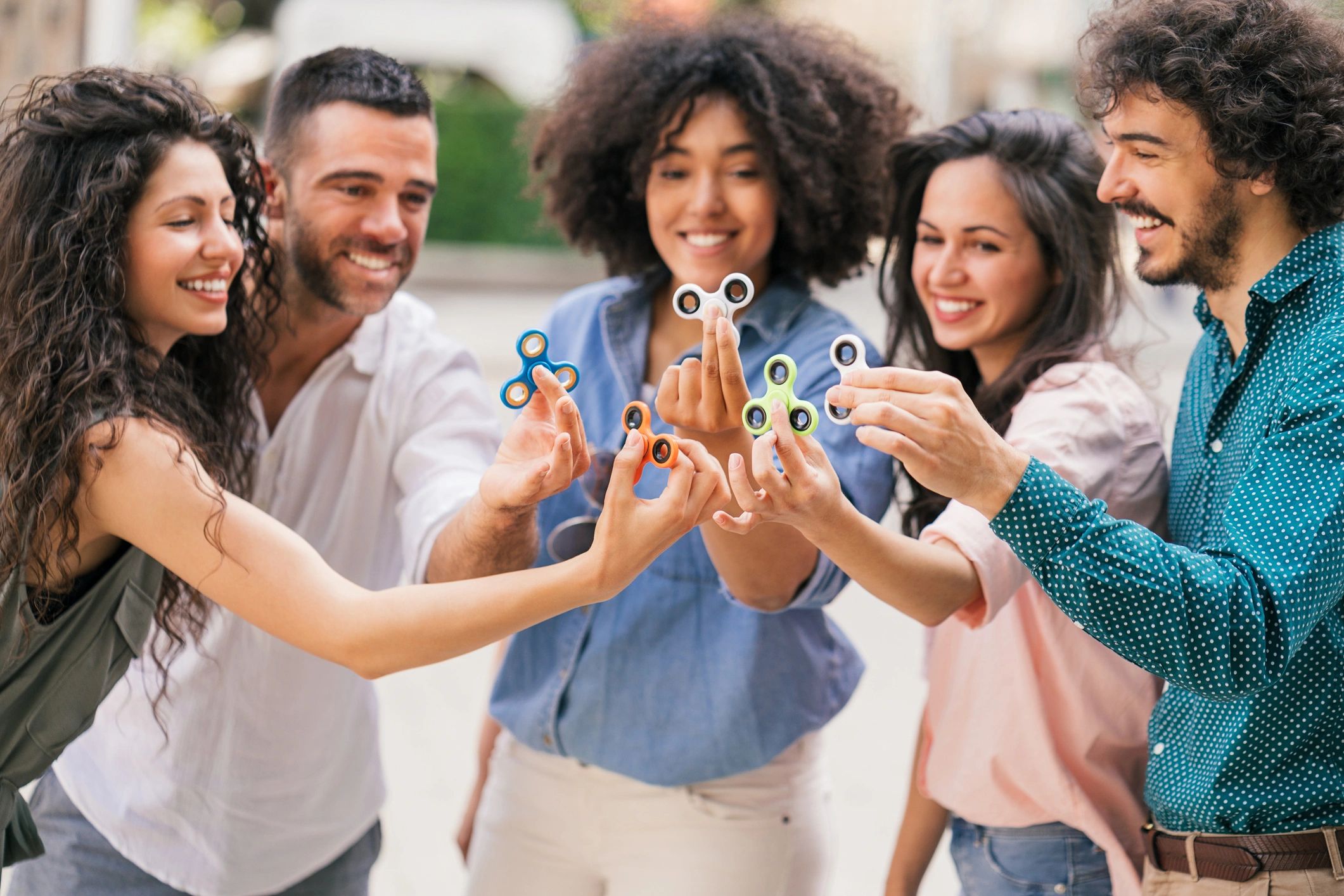 Five adults holding colourful 3D printed fidget spinners together outdoors