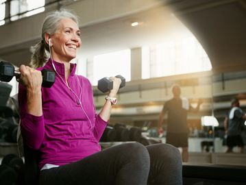 Smiling elderly woman lifting dumbbells at the gym.