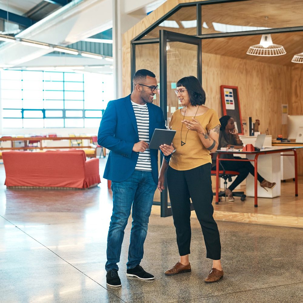 Two coworkers discussing a project on a tablet in a modern office space.