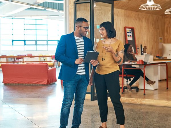 Two coworkers discussing a project on a tablet in a modern office space.