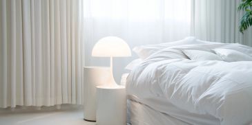Bright, minimalistic bedroom with white bedding and modern lamp.