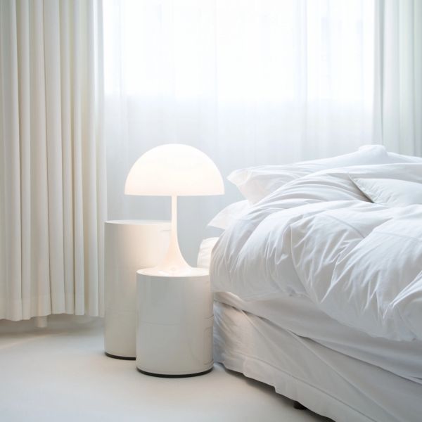 Minimalist bedroom corner with white lamp and bedding.