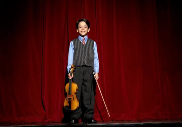 Young boy dressed formally holding a violin on stage.