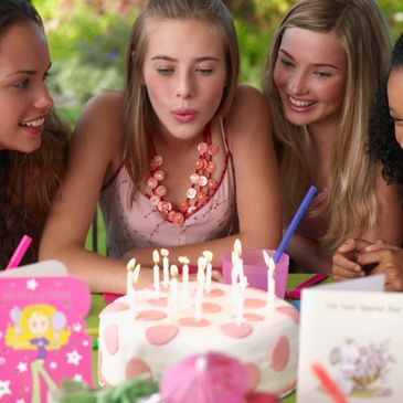 Teen girl blowing out birthday candles surrounded by friends.
