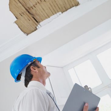Inspector in a blue helmet examining damaged ceiling with a clipboard.