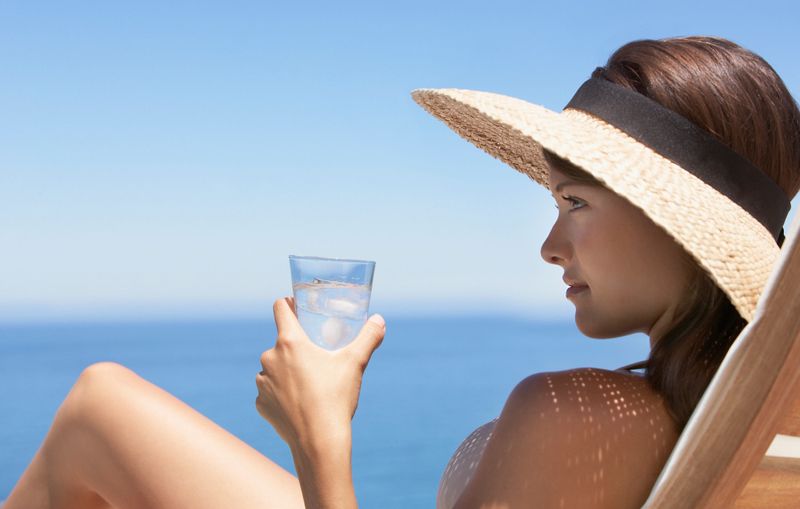 Woman in straw hat sunbathing on wooden chair with beverage