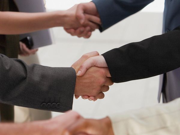 Multiple businesspeople shaking hands in formal attire, symbolizing agreement and partnership.