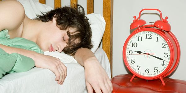 Person sleeping next to a large red alarm clock showing 3:45.