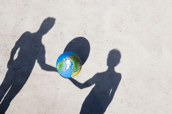 Shadows holding a globe between them on a concrete floor.